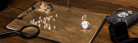 Panoramic shot of gemstones and jewelry with magnifying glasses on board on wooden table