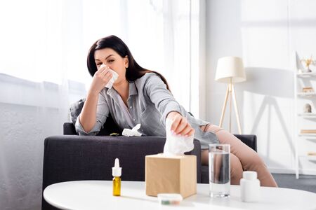 selective focus of allergic woman with running nose taking napkin near glass of waterの写真素材