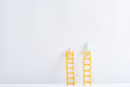 Plastic people figures on ladders on white surface on grey background, concept of equality rightsの写真素材