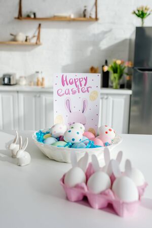 selective focus of painted chicken eggs near decorative bunnies and greeting card with happy easter letteringの写真素材