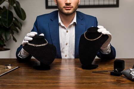 Cropped view of jewelry appraiser holding necklace stands with necklaces near jewelry on table in workshopの写真素材