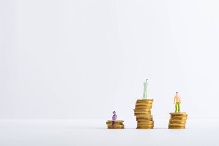 Three people figures on stacked coins on white surface isolated on grey, concept of financial...
