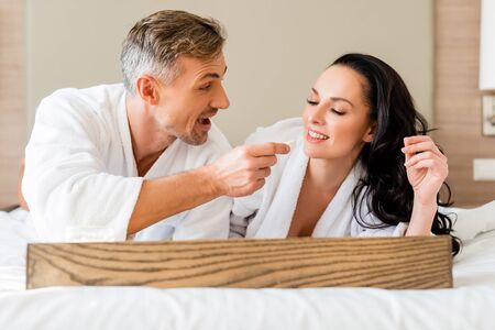 smiling boyfriend feeding attractive girlfriend with cheese in hotel