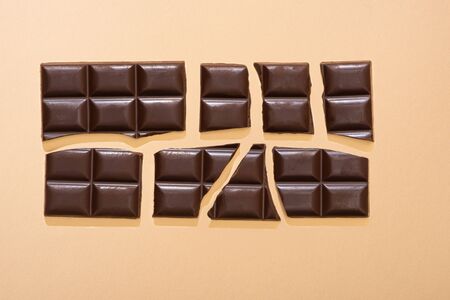 top view of delicious broken dark chocolate bar on beige background