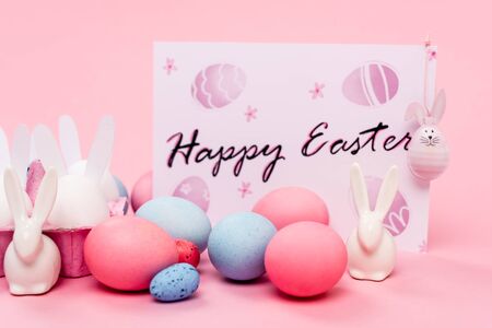 Colorful eggs, decorative bunnies and card with happy easter lettering on pink backgroundの写真素材