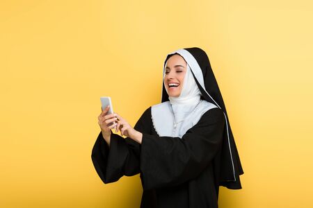 beautiful excited nun using smartphone on yellowの写真素材