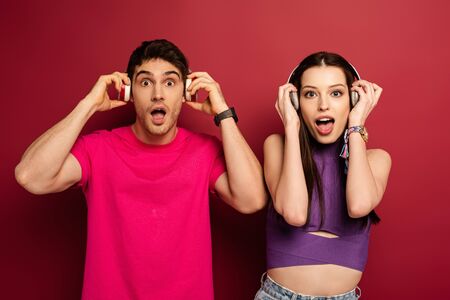 excited couple listening music with headphones on red