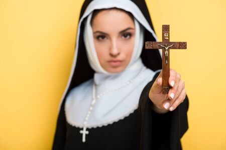 selective focus of beautiful nun holding cross isolated on yellowの写真素材