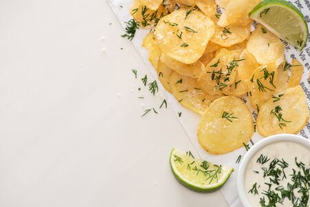 top view of potato chips with salt near sliced lime and garlic sauce on whiteの写真素材