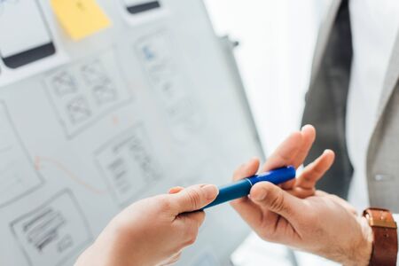 Cropped view of ux designer giving marker to colleague near project of ux design on whiteboard on...