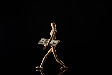Wooden doll imitating walking with dollar banknotes on black backgroundの写真素材