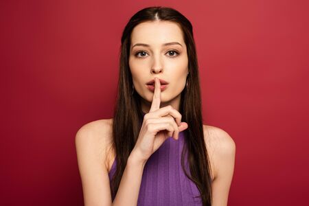 portrait of beautiful woman showing silence symbol on red