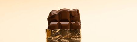delicious milk chocolate bar in golden foil isolated on beige, panoramic shot