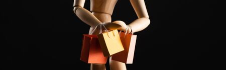 Wooden doll with shopping bags isolated on black, panoramic shotの写真素材