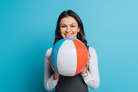 happy businesswoman holding inflatable ball while smiling at camera on blue backgroundの写真素材