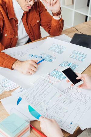 Cropped view of ux designers using smartphone and planning app frameworks for mobile website at...