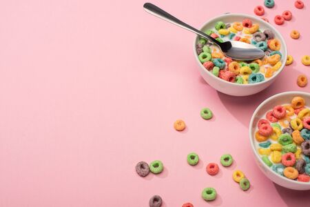 bright colorful breakfast cereal with milk in bowls with spoon on pink background