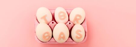 High angle view of chicken eggs with easter lettering in egg tray on pink, panoramic shot