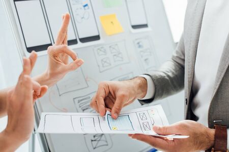 Cropped view of designer showing okay gesture near colleague with layouts of ux design near...