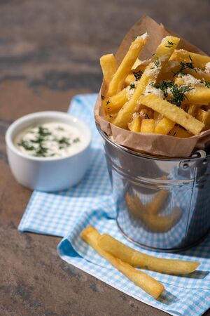 selective focus of bucket with salty french fries and creamy garlic sauce on marble surfaceの写真素材