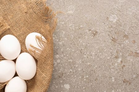 top view of white chicken eggs on sackcloth on grey cement backgroundの写真素材