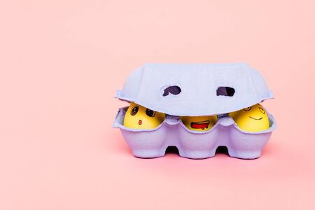 Easter eggs with funny facial expressions in egg tray on pinkの写真素材