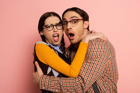 couple of frightened nerds in eyeglasses hugging on pink