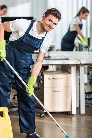 smiling cleaner looking at camera while washing floor in officeの写真素材