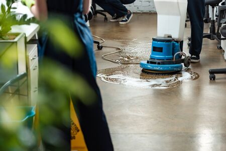 cropped view of cleaner washing floor with cleaning machine near colleaguesの写真素材