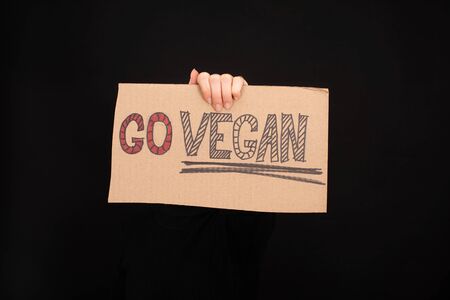 partial view of woman holding cardboard sign with go vegan inscription isolated on black
