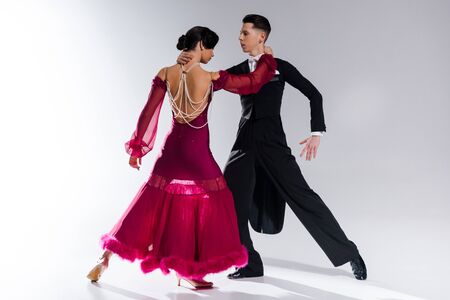 elegant young couple of ballroom dancers in red dress in suit dancing on whiteの写真素材