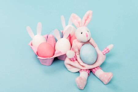 Pink egg tray with painted chicken eggs and decorative bunnies on blue, easter concept