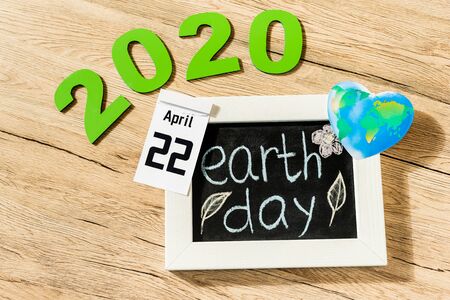 High angle view of board with earth day lettering, calendar with 22 april 2020 inscription and globe...