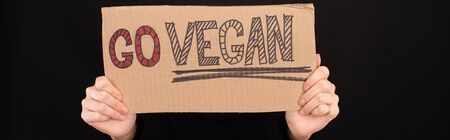 panoramic shot of woman holding cardboard sign with go vegan inscription isolated on blackの写真素材