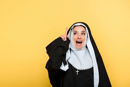 beautiful excited nun pointing up, on yellowの写真素材