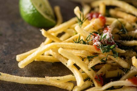close up of tasty french fries with ketchup, salt and dill near sliced lime