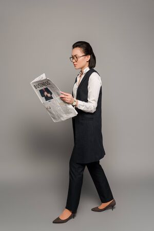 young businesswoman in eyeglasses reading newspaper on grey backgroundの写真素材