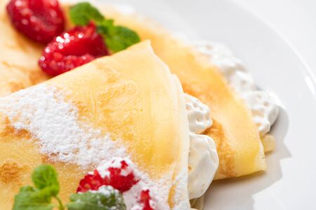 close up view of tasty crepes with raspberries and whipped cream on plateの写真素材