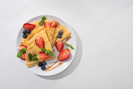 top view of tasty crepes with blueberries, strawberries and mint on plateの写真素材