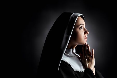 beautiful young nun looking up while praying with cross on greyの写真素材