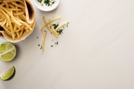 top view of crispy french fries, garlic sauce and sliced lime on white