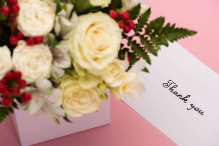 selective focus of bouquet of flowers in festive gift box near thank you greeting card on pink backgroundの写真素材