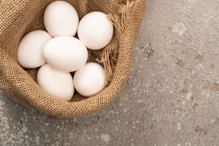 top view of white eggs in sackcloth on grey concrete background