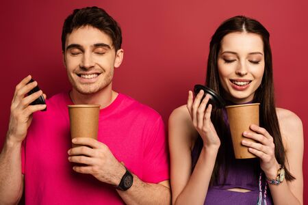 beautiful happy couple smelling coffee in disposable cups on redの写真素材