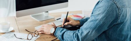 Cropped view of ux developer using graphics tablet and computer near sketches on table, panoramic...