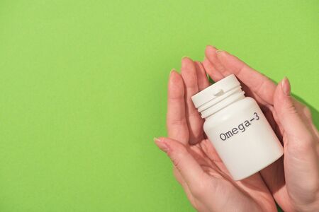 Cropped view of woman holding container with omega-3 lettering on green backgroundの写真素材