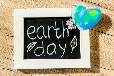 Top view of board with earth day lettering and globe on wooden background