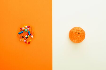 Top view of colorful pills and mandarin on white and orange background