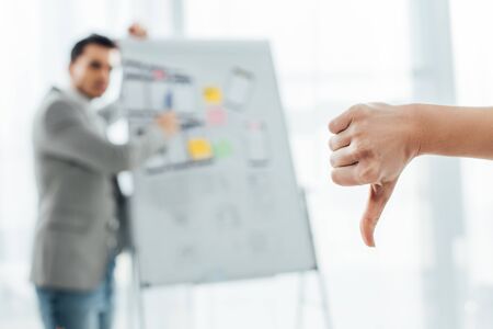 Selective focus of ux designer showing dislike sign to colleague near whiteboard in office