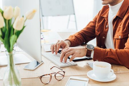 Cropped view of developer using computer near templates of ux design and coffee on tableの写真素材